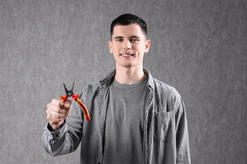 Poster - Young man holding pliers on grey background