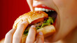 ハンバーガーを食べる女性の口元 赤色背景