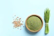 Wheat grass powder in bowl, seeds and fresh sprouts on light blue background, flat lay