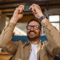 Wall Mural - Adult man with eyeglasses play video games on his phone at home