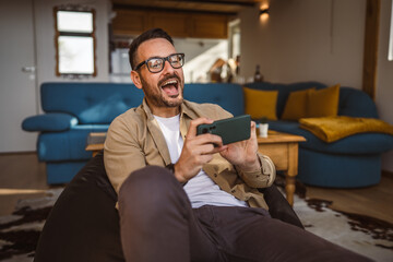 Wall Mural - Adult man with eyeglasses play video games on his phone at home