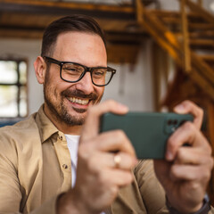 Wall Mural - Adult man with eyeglasses play video games on his phone at home