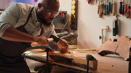 Sticker - African american sculptor shaping raw timber using chisel and hammer in carpentry shop, creating wood art, wearing safety glasses. Artist making wood sculptures, engraving lumber with tools, camera A