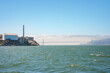 View of Alcatraz Island in San Francisco Bay, CA, USA. The Federal prison buildings and the Golden Gate Bridge are visible in the backdrop, creating a contrast between nature and history.