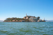 Sunny view of Alcatraz Island in San Francisco Bay, California, USA. Features former prison complex with main cellhouse, lighthouse, and serene waters.