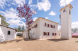 White facades of an Andalusian cortijo style country house with red wooden shuttered windows and terracotta and gravel floors on a clear sky day