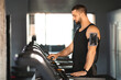 © Prostock-studio - A man wearing a black tank top is vigorously running on a treadmill in a gym setting. He is focused and determined, with his hands gripping the side rails for stability as he pushes his limits.