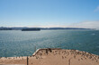 Scenic view from Alcatraz Island overlooking San Francisco Bay. Sandy area with birds, sparkling waters, cityscape, and Bay Bridge visible under clear skies.