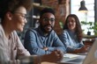 © Igor - Portrait of young african american businessman in eyeglasses sitting at table in modern office. Group of diverse businesspeople working together. Teamwork concept