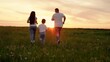 Dad baby mom play together in meadow. Family runs across meadow together toward sunset. Joyful parents enjoy getaway with young son in open air. Mother, father with child enjoy active life in nature.