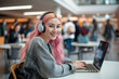 Engaging young woman with vibrant pink hair listening to music on her headphones while working on her laptop at a busy cafe, exuding positivity and modern lifestyle vibes