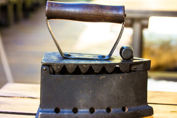 Vintage antique heavy cast iron retro iron with a wooden handle for ironing clothes is lying on a wooden table. Bric-a-brac collection at flea market. Retro technology, ancient steel tool for homework