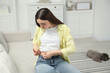 © New Africa - Diabetes. Woman making insulin injection into her belly on sofa at home
