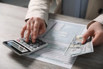 Wall Mural - Payroll. Woman with dollar banknotes and calculator planning budget at wooden table, closeup