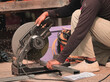 Worker using a sliding compound mitre saw with circular blade for cutting steel metal.