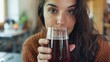 A woman holds up a glass of dark reddishbrown kombucha her face scrunched in anticipation of the taste.