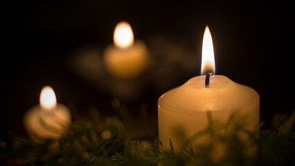 A large candle in focus and two candles in the background of the image. Three candles lit in the dark