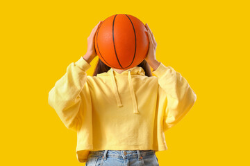 Young woman in hoodie with ball on yellow background