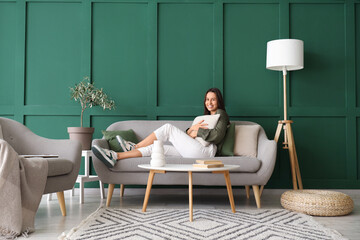 Wall Mural - Beautiful woman with cushion resting on grey sofa in living room