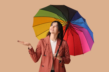 Wall Mural - Young woman with opened colorful umbrella on beige background