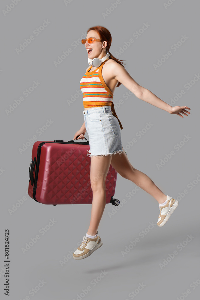 Female tourist with suitcase jumping on grey background