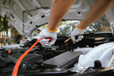 Fototapeta  - Close-up of auto mechanic charging car battery with electric rail jumper cables	