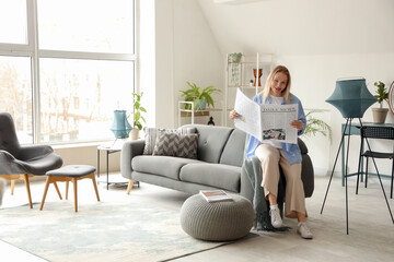 Wall Mural - Young woman resting on sofa and reading newspaper in white living room