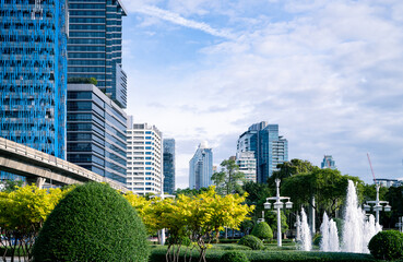 A city with tall office buildings and a central fountain. Sustainable cityscape surrounded by trees and bushes. Sustainable city design. Urban environment. Lush city park. Inside a green cityscape.