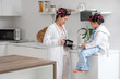 © Pixel-Shot - Young Asian woman pouring coffee and her little daughter with hair curlers in kitchen