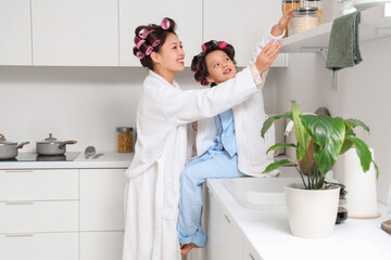 Poster - Little Asian girl and her mother with hair curlers in kitchen