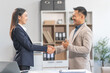 © Phushutter - Young Asian businesswoman and middle-aged businessman, exemplifying pivotal moments, clear articulation, proliferation of ideas, and overcoming divisive challenges with successful handshakes.