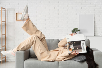 Wall Mural - Beautiful young woman with magazine lying on sofa at home