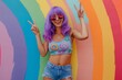 photo of happy woman with purple wig, wearing sunglasses and tank top with donut print on it, denim shorts, showing peace sign, rainbow background
