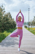Woman practicing yoga outdoors, performing a tree pose on a wooden walkway, serene and focused