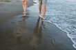 Down view of bare feet on sand beach. Couple in love walking barefoot on water with big waves on seashore. Man and woman walk on sea. Spending time together. Bottom view on legs. Back view.