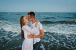 Swimming in clothes. Portrait of a beautiful man and woman wet in sea. Couple hugging and kissing in sea. Male kisses and hugs female standing on water with big waves ocean and enjoying a summer day.