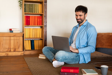 Aufkleber - A man is seated on the floor, typing on a laptop in front of him. He appears focused and engaged with the laptop screen, surrounded by a simple indoor setting.