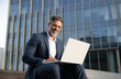 © Stock 4 You - Smiling mature successful businessman working, typing on laptop sitting outdoors at office building. 40s latin hispanic man entrepreneur in suit using wireless pc computer for online business invest
