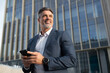 © Stock 4 You - Portrait of smiling executive ceo manager. Latin adult man in suit using smartphone application app device for business at office outdoors. Successful mid age senior businessman holding mobile phone.