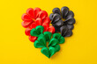 Overhead shot of miniature paper hearts arranged to create a grand heart shape, mirroring the hues of Juneteenth - red, green, black against a vibrant yellow backdrop, perfect for social messages