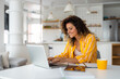 © Dorde - Beautiful smiling young woman working on laptop in her home office wearing stripped yellow shirt.