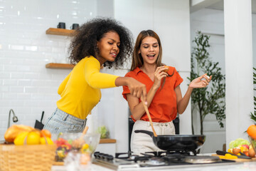 Wall Mural - Diversity young happy love LGBT, LGBTQ caucasian and african family lesbian couple woman cook vegan food healthy eat with fresh vegetable salad in kitchen at home, pride, rainbow.Lgbt lesbian couple