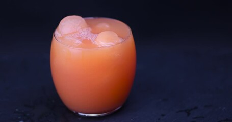 Wall Mural - grapefruit juice with ice in a glass on a black background, a glass with cold grapefruit juice