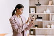 Focused professional woman in a pink blazer using a smartphone in a modern office, embodying efficiency and modern workplace aesthetics