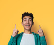 Excited black curly haired man in braces, open mouth, wear green denim shirt advertise pointing show area for sales slogan text, isolated yellow over wall background. Dental care, ad concept.