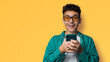 Excited surprised shocked astonished happy curly haired funny young man wear braces sunglasses glasses open mouth hold typing cell phone cellular smartphone, isolated yellow background