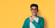 Excited happy curly haired man in braces, open mouth, wear sunglasses glasses green shirt advertise show point area for sales slogan text, isolated yellow background. Dental care ophthalmology ad.