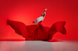 Passionate woman, flamenco dancer in stylish costume with skirt spreads like wings, performing against vivid red background. Concept of art of movement, classical dance, beauty, festival