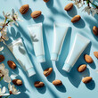 Five white cosmetic tubes symmetrically arranged on a pale blue surface amidst scattered almonds and white flowers