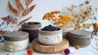 Elegant ceramic scrub jars filled with natural skincare products on wooden display surrounded by dried flowers
